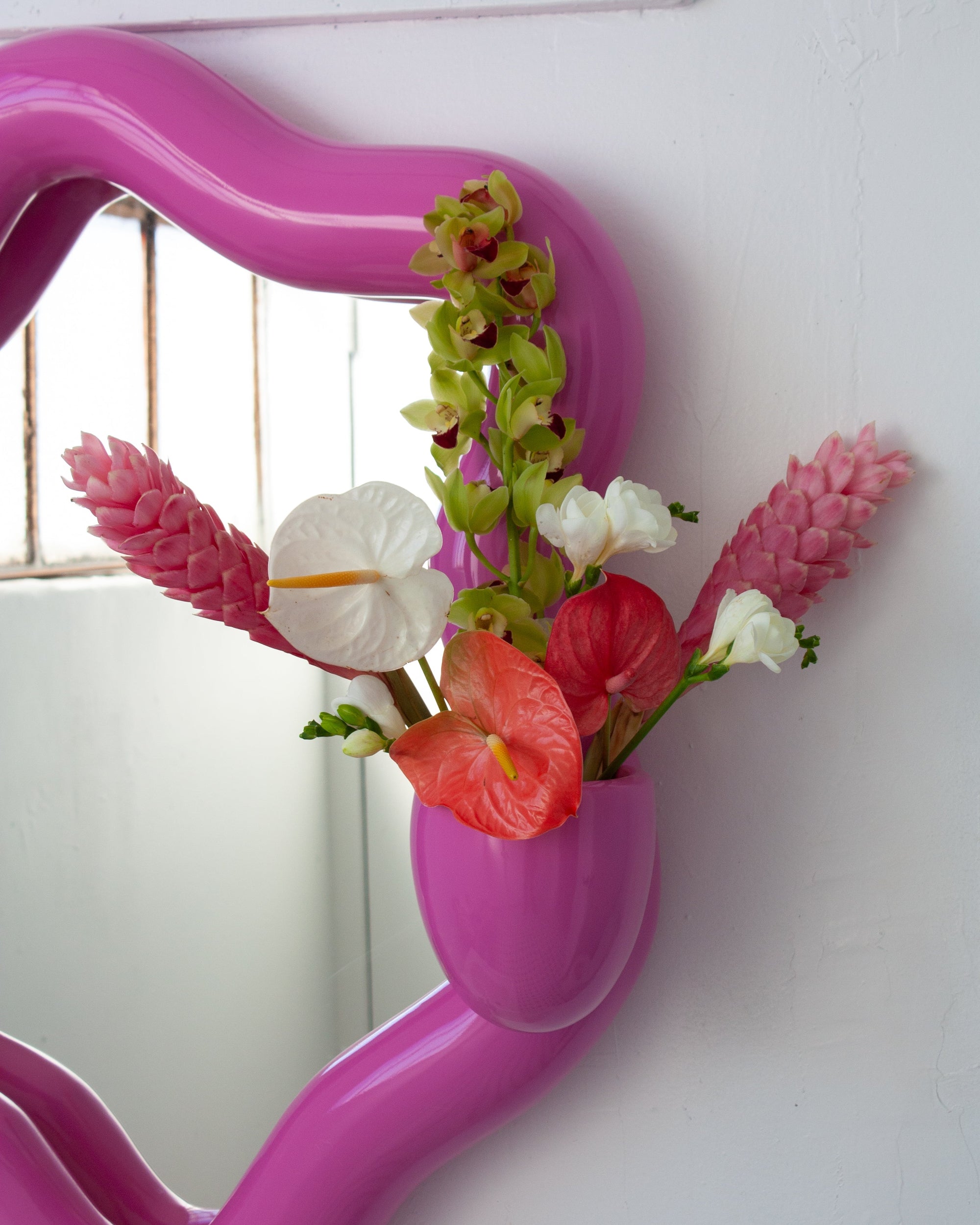 Pink mirror with floral arrangement on a white wall