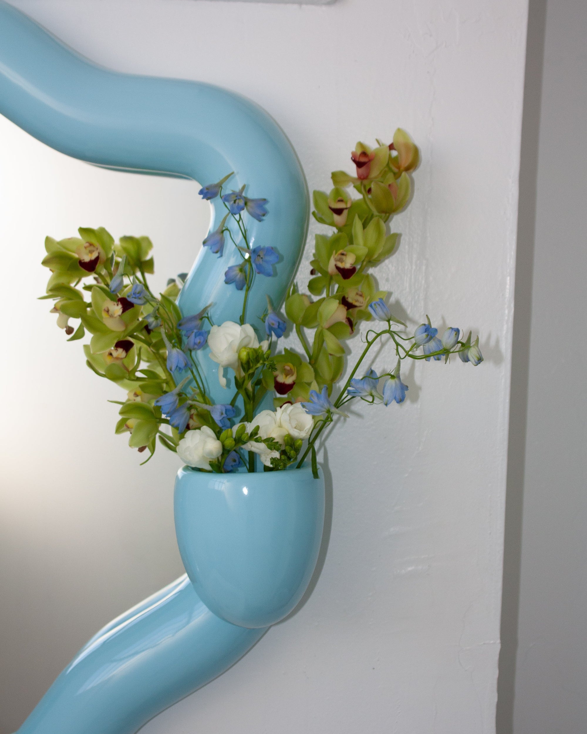 Blue vase with flowers attached to a white wall